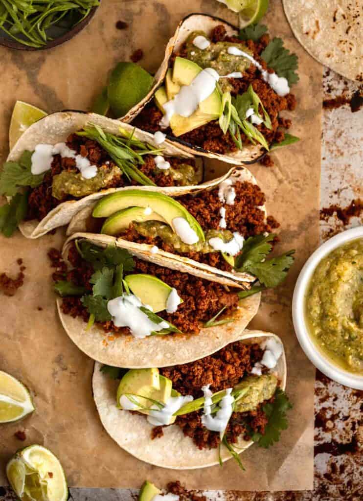 The best chorizo tacos on a tray with cilantro and a bowl of salsa verde to the side.