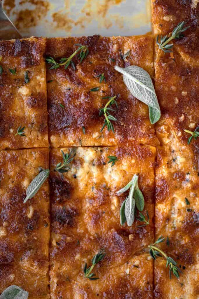 homemade sweet potato au gratin in a baking dish that's been cut into squares. Two of the squares are removed from the dish. Fresh sage leaves and fresh thyme are on top as a garnish.
