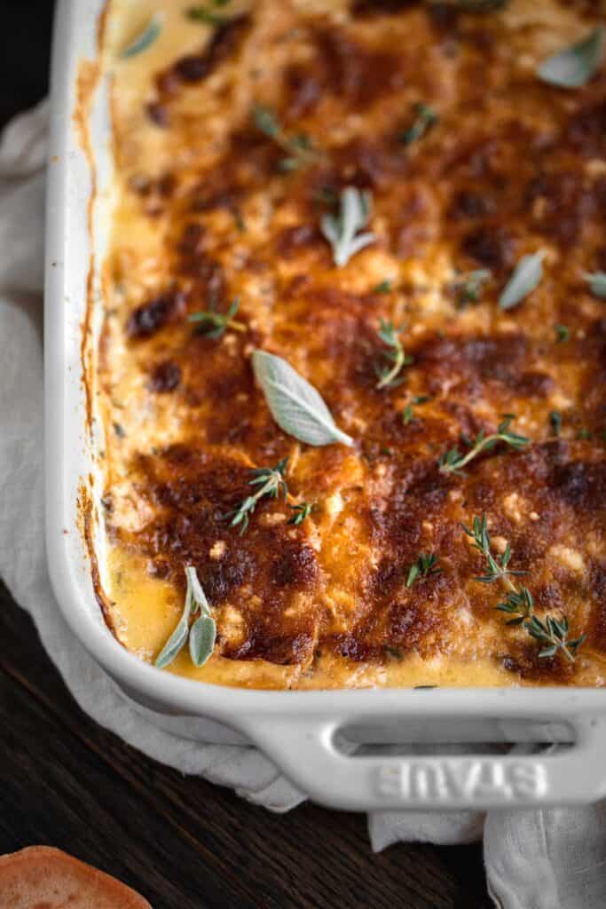 Baked sweet potato au gratin right out of the oven topped with fresh sage and thyme.