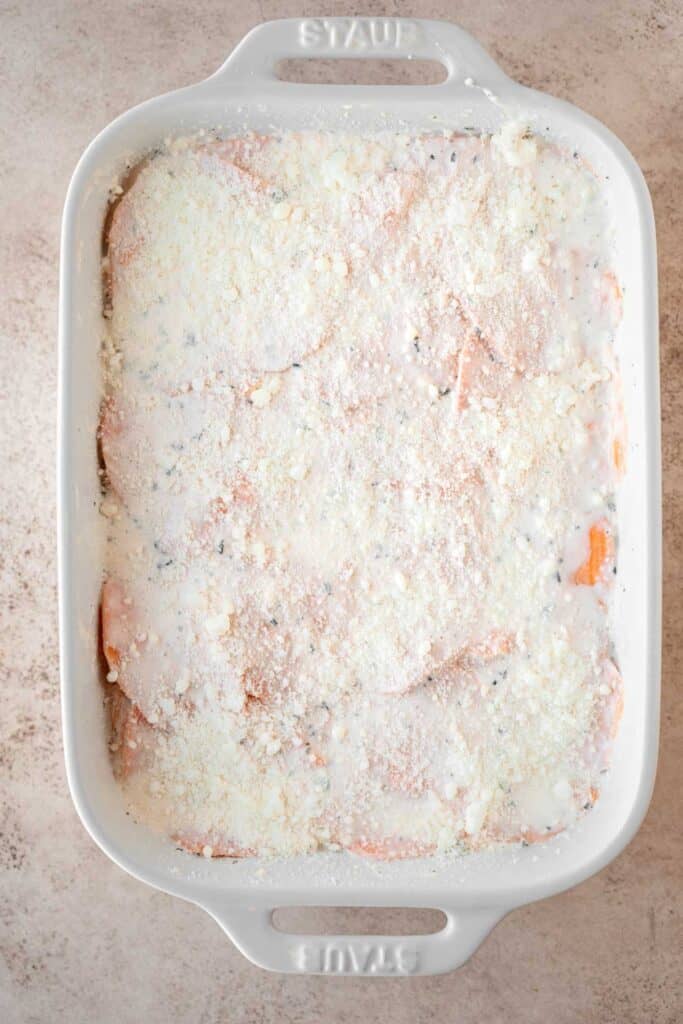 Sweet potato slices completely covered in cream then topped with Romano cheese in a white baking dish right before going into the oven.