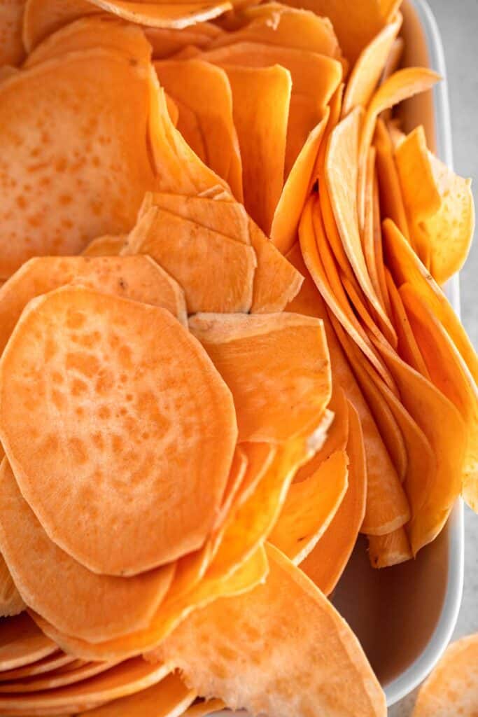 Raw sweet potato slices that are about 1/8 inch thick in a white baking dish.