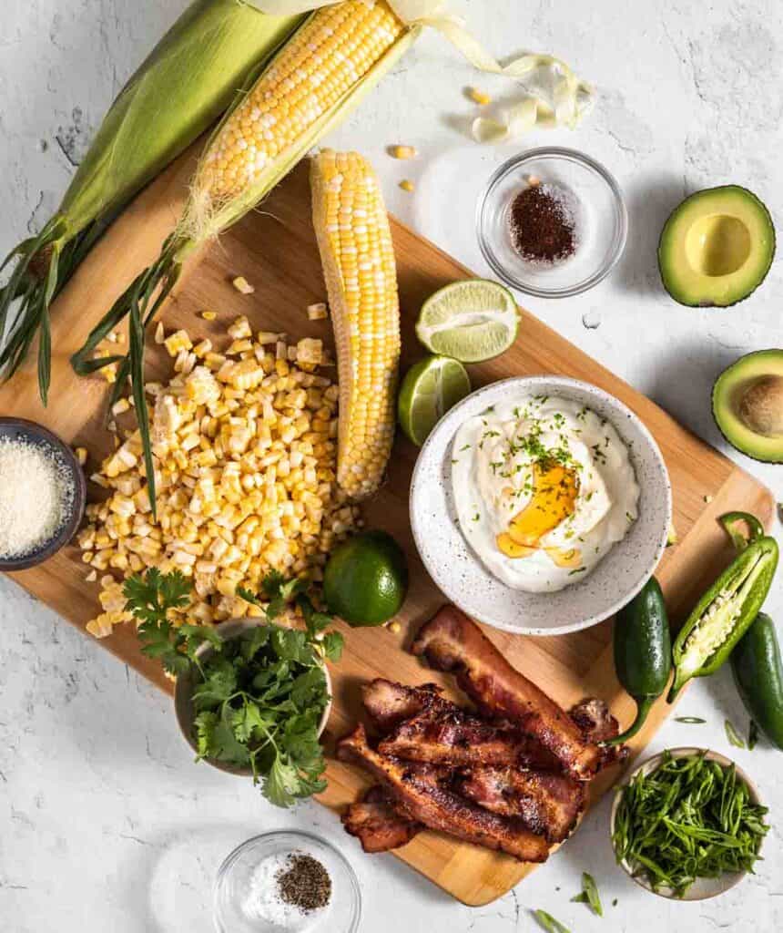 Corn cobs with some corn cut off, cotija cheese, green onions, bacon, cilantro, jalapeno, limes, dressing, avocado and spices.