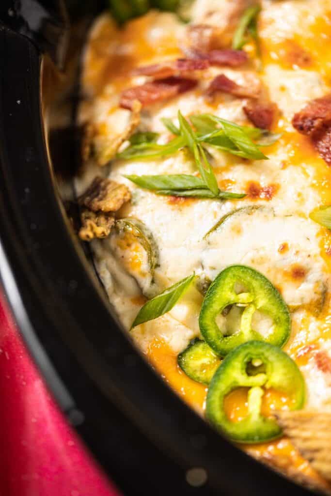 A close up of the jalapeno dip in the crock pot topped with fresh jalapenos, bacon and green onions.