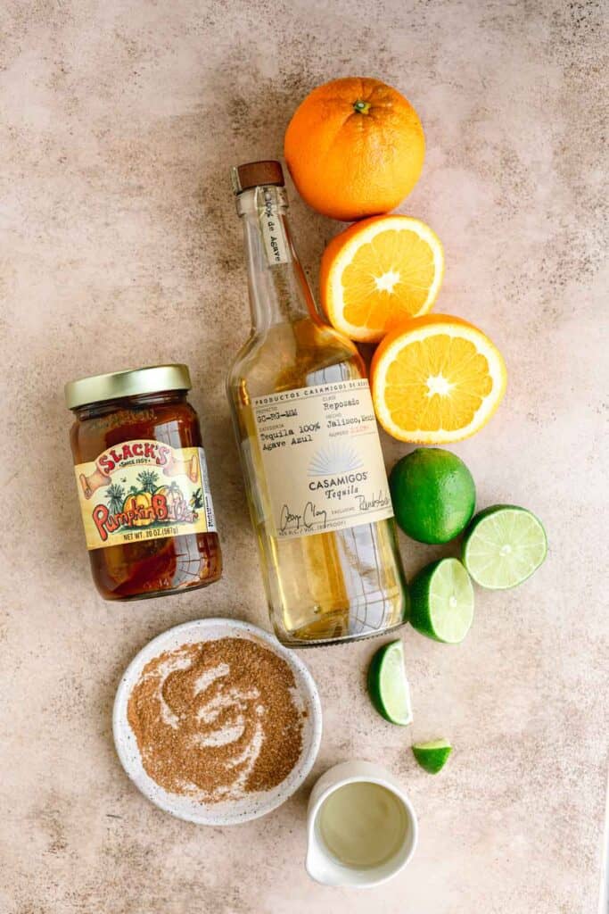 Casamigos reposado tequila, oranges, limes, simple syrup, pumpkin spice with salt on a plate and a jar of pumpkin butter. 