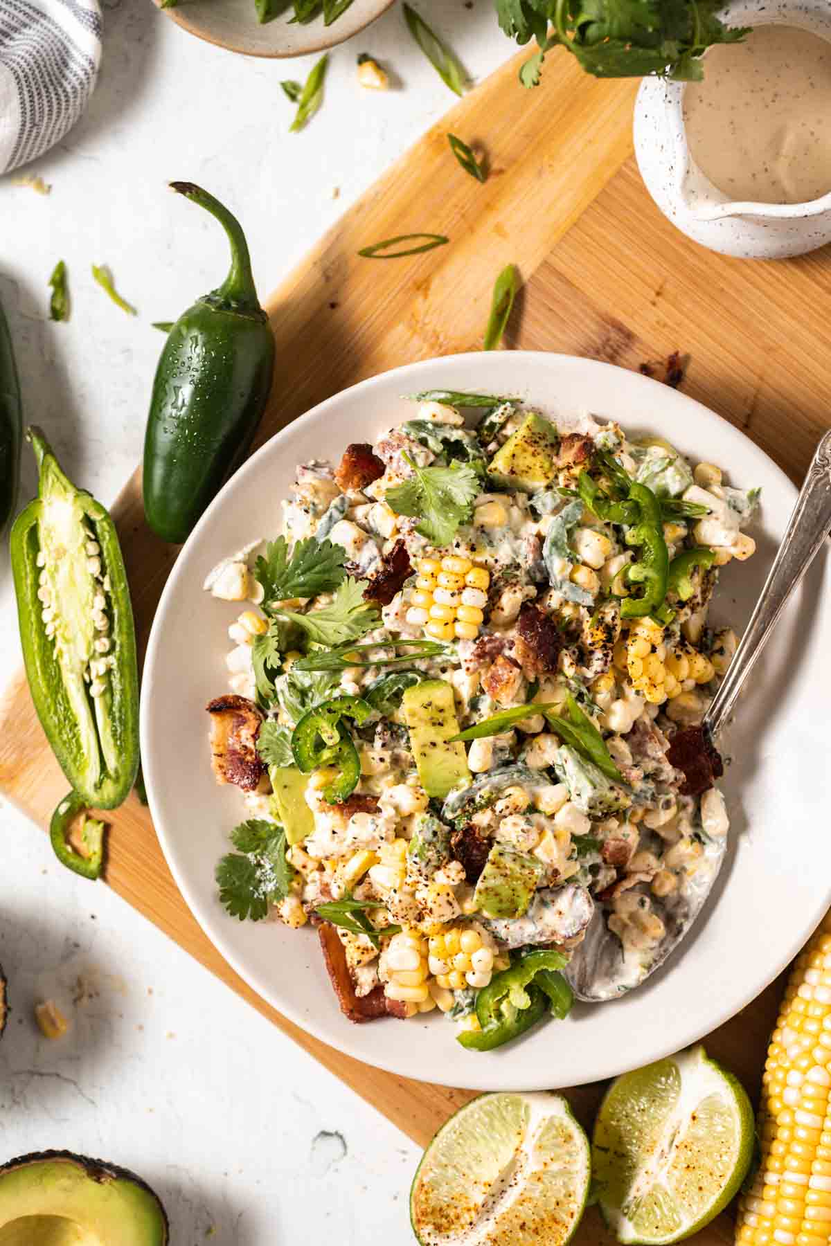 Corn salad with bacon, lime, avocado, cilantro and jalapeno in a bowl with a serving spoon.