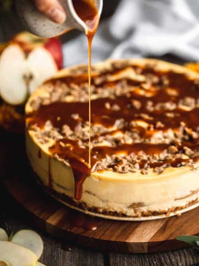 Caramel sauce being drizzled on top of the Apple Pie Stuffed cheesecake on a wooden circular serving dish.