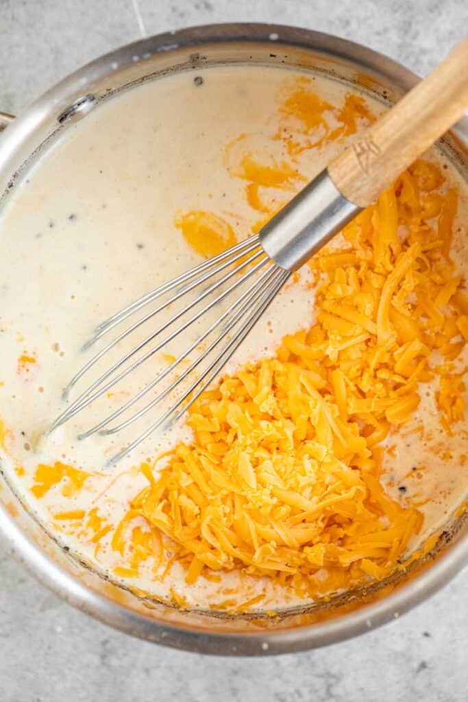 Shredded cheddar cheese, seasonings and evaporated milk in a medium sauce pot with a whisk.
