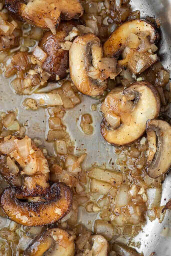 Mushrooms and onions being sauteed in a large skillet.