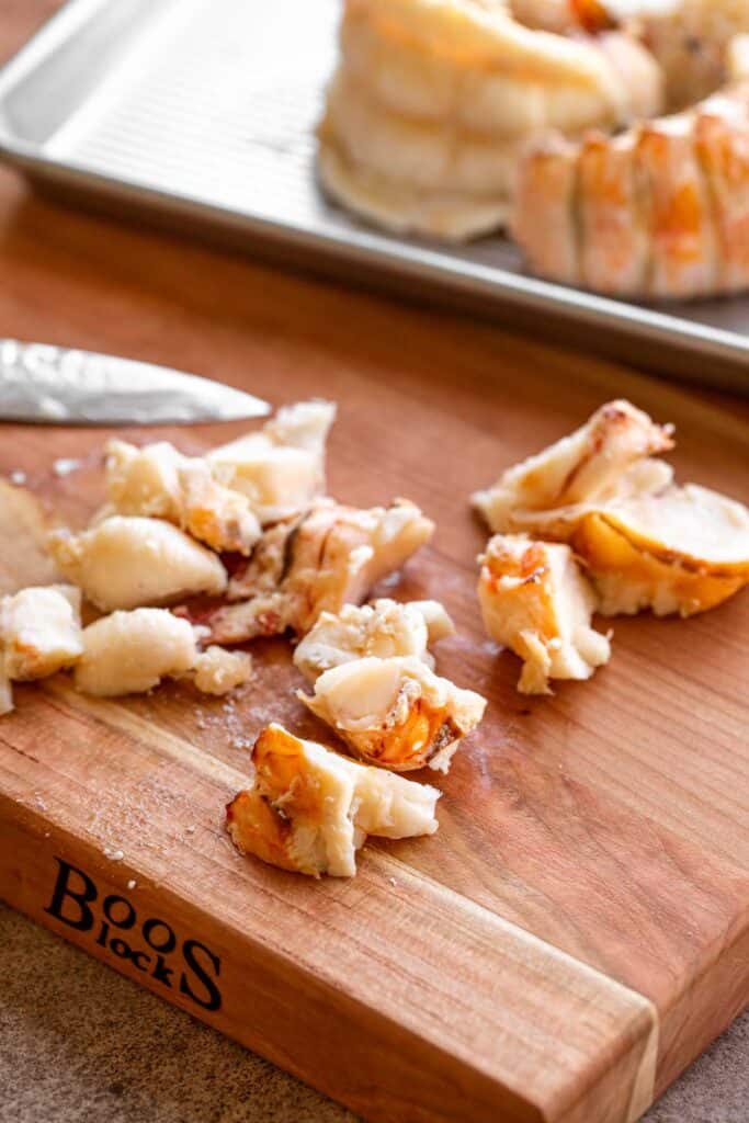 Lobster meat being cut into 1 inch pieces on a wooden Boos Block cutting board.