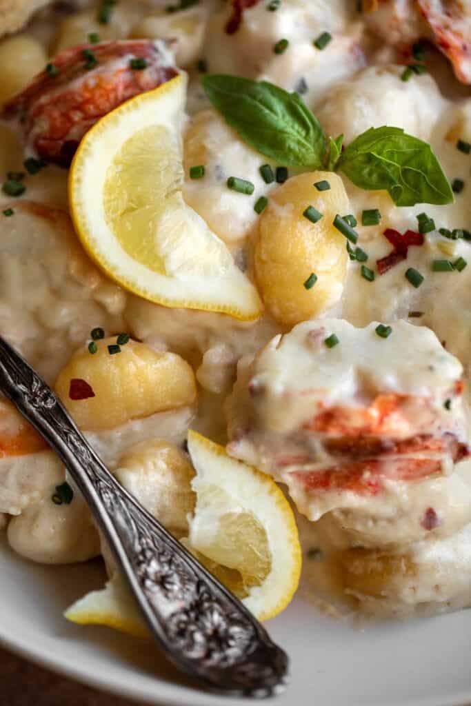 Close up of gnocchi, lobster, lemon and basil in a bowl covered in parmesan cream sauce with a fork in the bowl. 