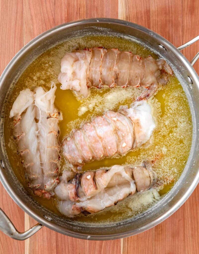 Lobster tail meat cooking in a large pan of butter. 