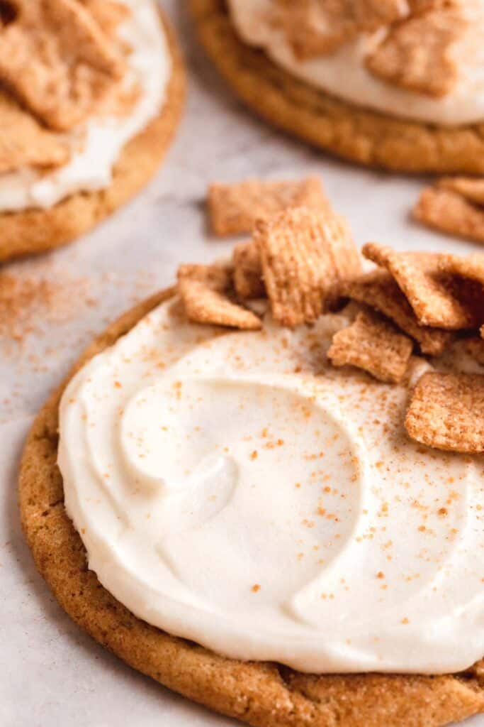 Cinnamon Toast Crunch Cookie with cream cheese frosting swirled on top and pieces of cereal.
