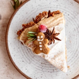Gingerbread Cream Pie slice on a white plate with a gingerbread cookie, star anise and cranberry on top for garnish.