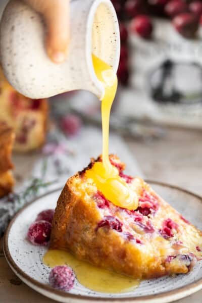 A slice of Christmas cranberry cake with butter sauce being poured onto the top of it.