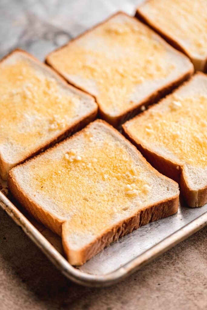 Garlic butter spread over Texas toast on a sheet pan.