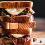 Texas Toast Sloppy Joes stacked on top of each other on a wooden cutting board with melting cheese coming over the edge of the sandwich.