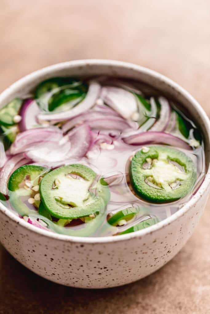 Pickled red onion and jalapeno in a white speckled bowl. 