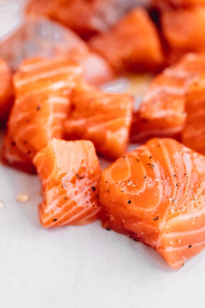 Raw salmon seasoned with salt, pepper, oil and honey on a parchment lined sheet tray.