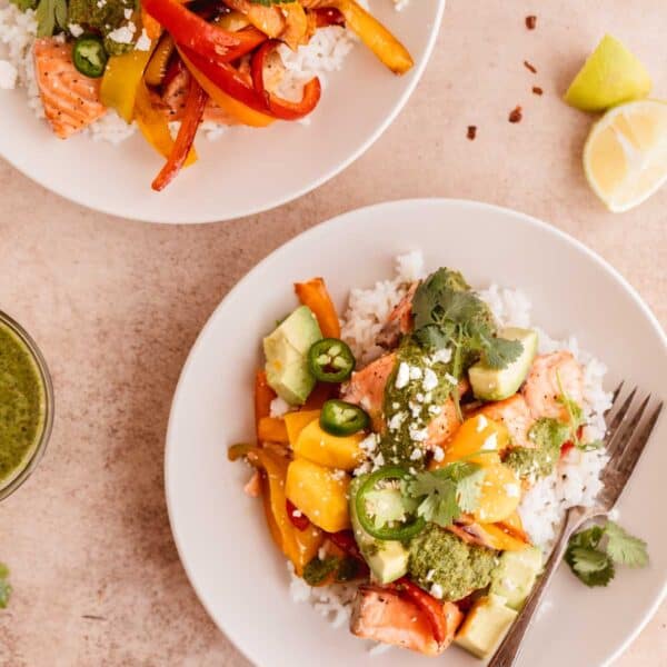 Salmon and rice bowl with mango, avocado, peppers, chimichurri and lime in off white bowls.