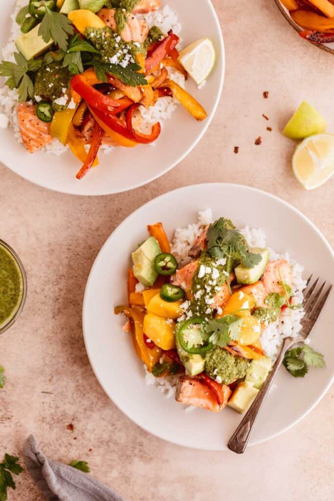 Salmon and rice bowl with mango, avocado, peppers, chimichurri and lime in off white bowls.