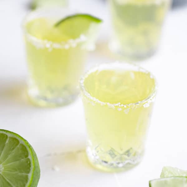 3 shot glasses filled with a green tea shot, salt on the rim and a lime wedge on one glass.