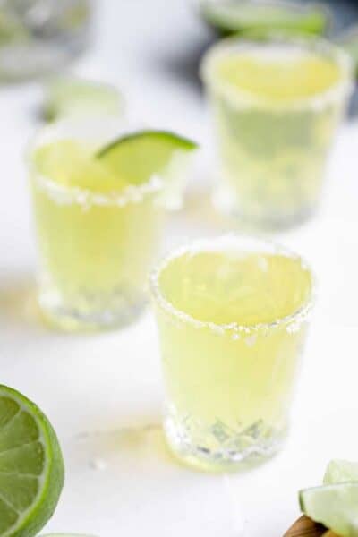 3 shot glasses filled with a green tea shot, salt on the rim and a lime wedge on one glass.