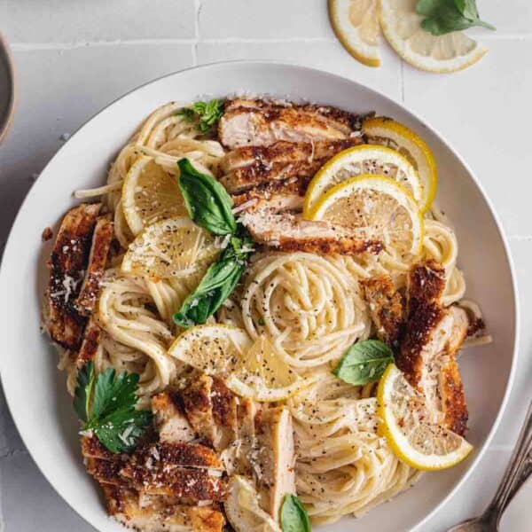 Lemon chicken pasta recipe fully made in a large bowl, topped with lemon slices.