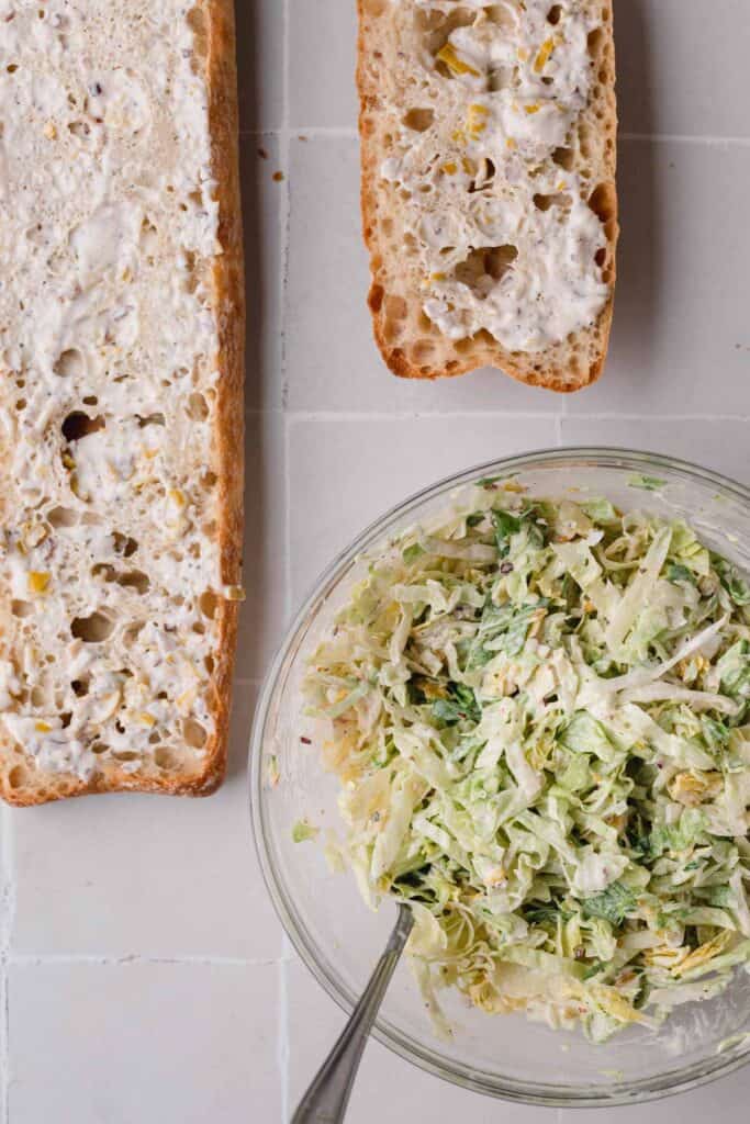 Dressing smeared on cut bread, lettuce salad mixed in a bowl.