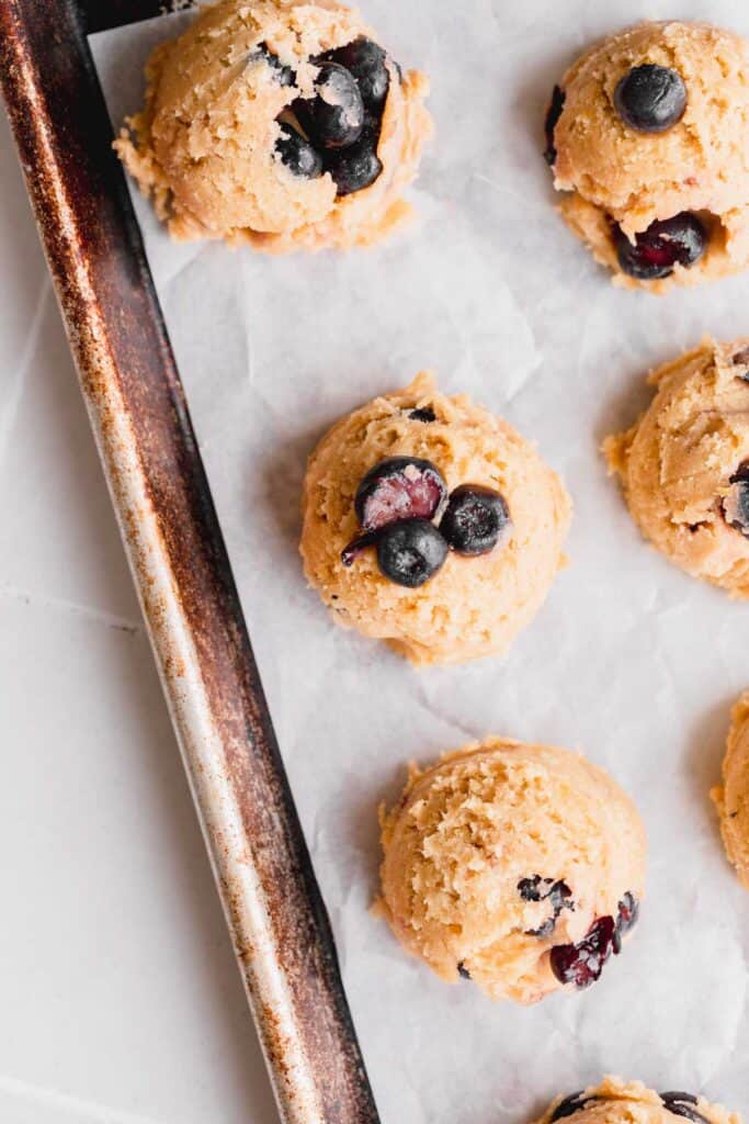 Cookies on a sheet pan with blueberries on top of them.