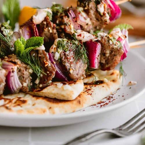Garlic Herb Lamb Kabobs with red onion and dill on a plate with naan and a fork lying next to it.