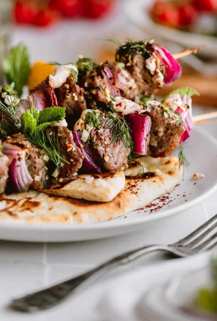 Garlic Herb Lamb Kabobs with red onion and dill on a plate with naan and a fork lying next to it. 
