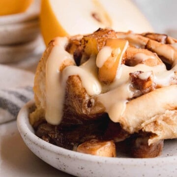 One cinnamon roll on a plate with butter sauce over the top.