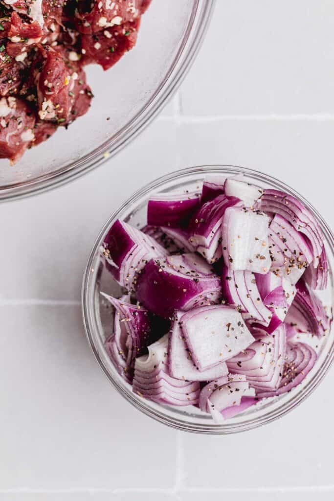 Red onions in a glass bowl with olive oil, salt and pepper. 