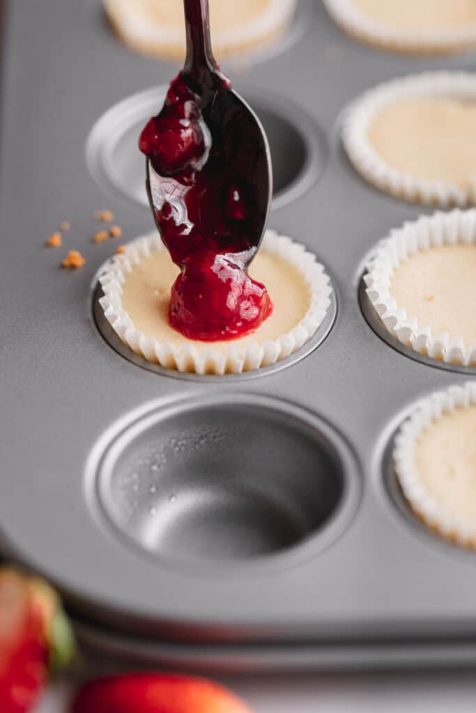 A small spoonful of compote being spooned onto a mini cheesecake.