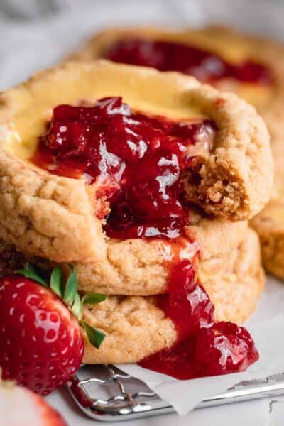 Strawberry cheesecake cookies stacked up with strawberry compote running down the front and a strawberry next to them.