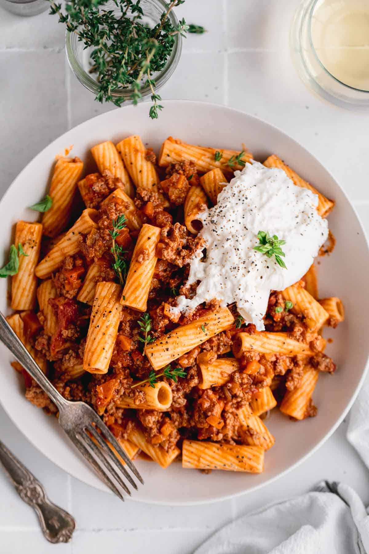Rigatoni Bolognese with burrata in a bowl with a fork.