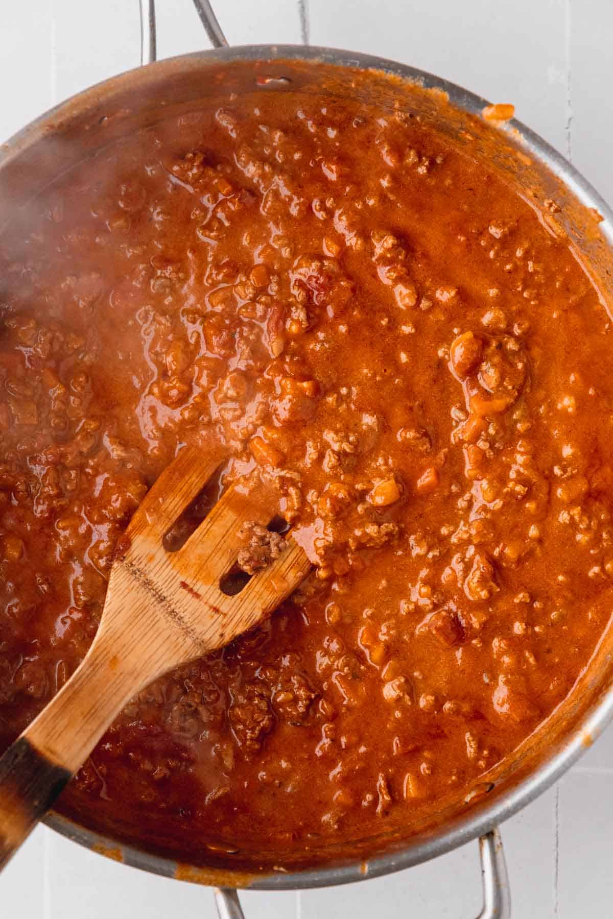 Bolognese sauce simmering in a pan with a wooden spatula.