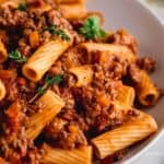 Rigatoni Bolognese in a white pasta bowl, garnished with fresh thyme.
