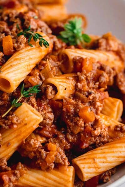 Rigatoni Bolognese in a white pasta bowl, garnished with fresh thyme.