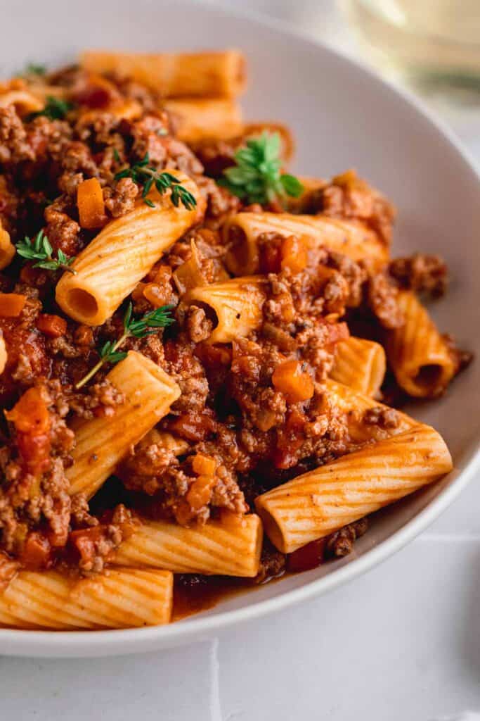 A bowl of rigatoni bolognese with fresh thyme.