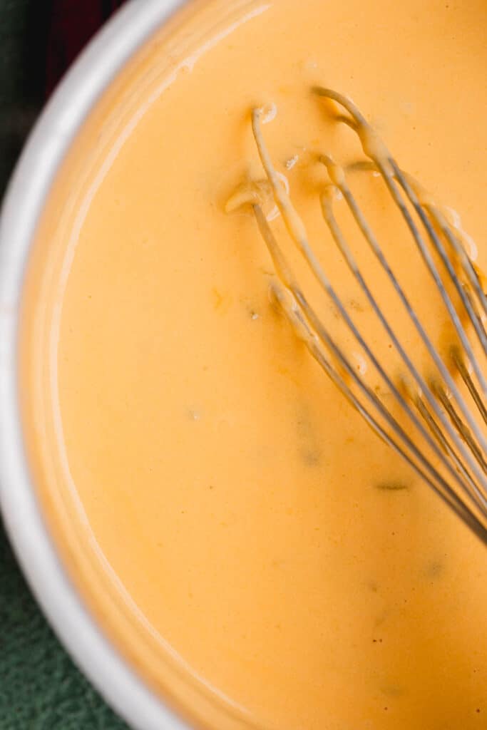 Creamy homemade cheese sauce in a pot with a whisk. 