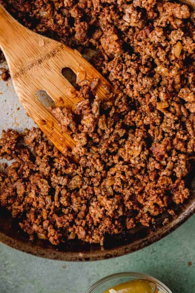 Cooked ground beef with taco seasoning in a pan with a wooden spatula. 