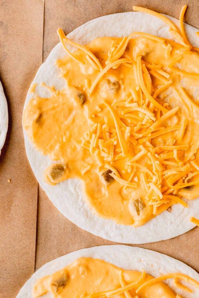 Cheese sauce and shredded cheese spread on a flour tortilla. 