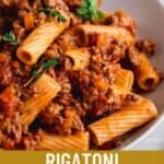 Rigatoni Bolognese in a large white pasta bowl, garnished with fresh thyme.