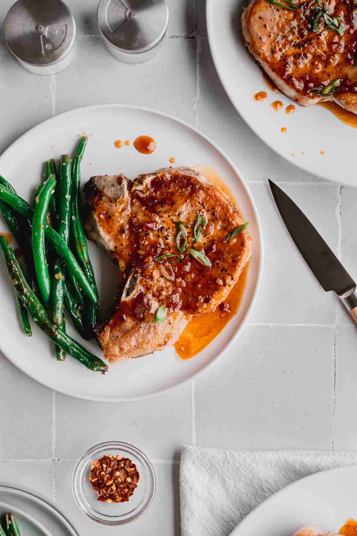 Honey Garlic Pork Chop recipe on a plate with green beans and a knife to the side. 