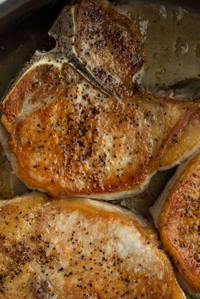 Seared pork chops in a large skillet. 