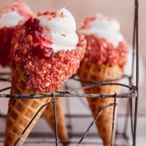 Strawberry crunch cheesecake cones topped with strawberry compote in a wire rack.