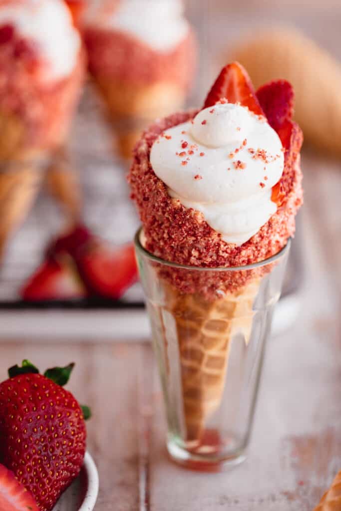 A strawberry crunch cheesecake cone held up in a small glass cup.
