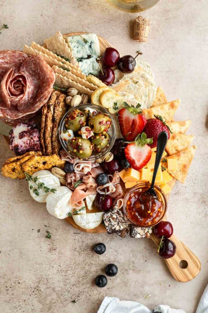 A small charcuterie board with meat, cheese, jam, fruit and olives.