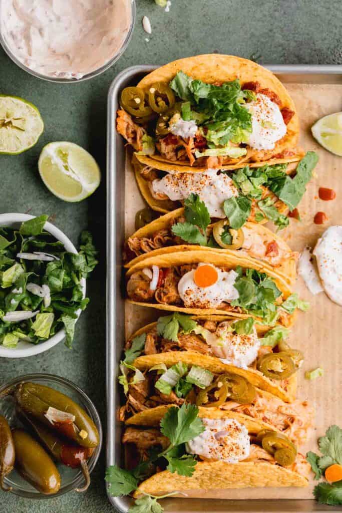 Baked chicken tacos on a sheet tray, loaded with toppings.